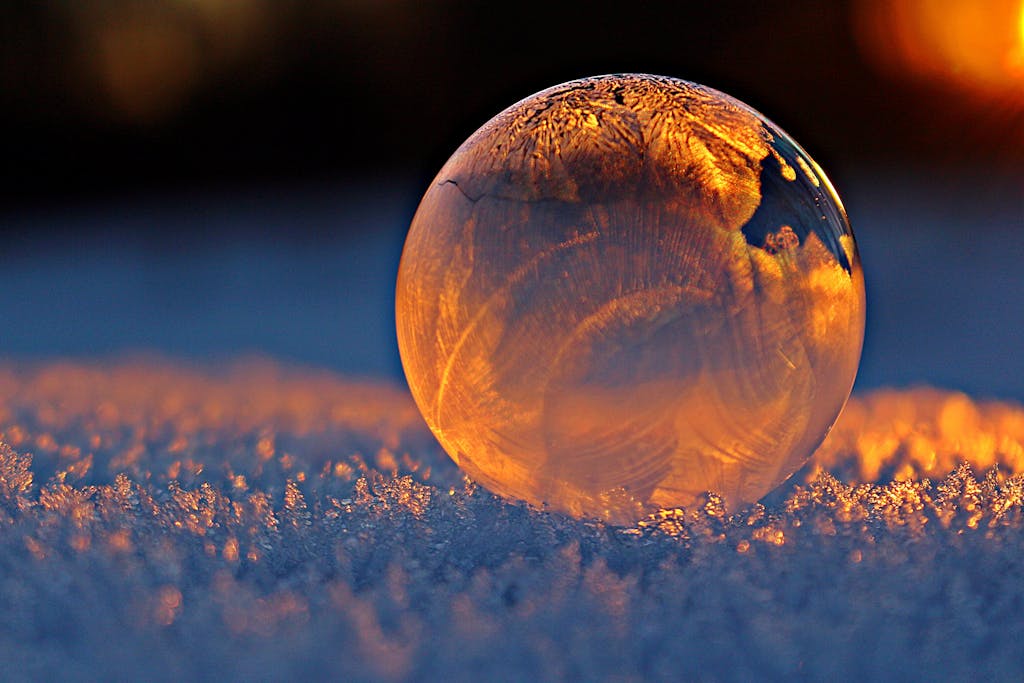close up shot of a frozen bubble with warm reflections resting on a snowy surface at twilight. 302743 scaled